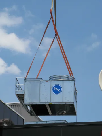 A cooling tower being lifted by a crane into a high-rise office building