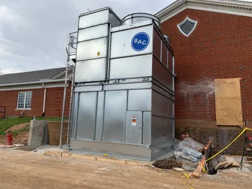 A cooling tower being installed outside of a brick building