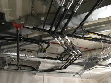 An open ceiling showing a network of air ducts and refrigerant lines