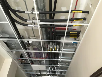 A drop ceiling before panels installed revealing tightly packed air ducts and insulated refrigerant lines