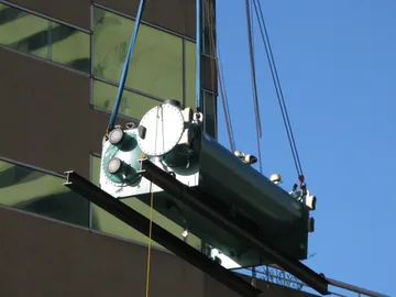 A boiler being lifted by a crane up to a high-rise office building